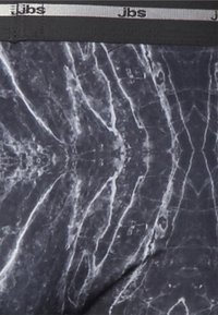 Sort stof med et marmor-lignende mønster i grå og hvid. Har en sort elastisk talje med "Jbs" branding.