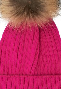 Berretto lavorato a maglia rosa con texture a coste e un grande pompon in pelliccia sintetica di un marrone chiaro a contrasto sulla parte superiore.