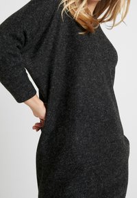 Robe pull gris foncé fabriquée dans un tissu doux et texturé, avec des manches longues, une coupe ample et des poches latérales.