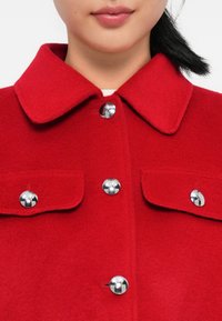Czerwona kurtka z wełny z kołnierzem, z srebrnymi zapięciami na napy i dwoma kieszeniami z klapkami, oferująca gładką fakturę i zorganizowany krój.