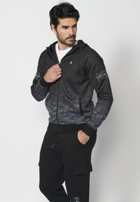 Čierna a sivá gradientná mikina so zipsom, kapucňou, prednými vreckami a elastickými manžetami, s logom na ľavom rukáve.