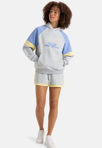 Gray hoodie with blue and yellow accents, featuring a graphic logo. Paired with gray shorts, both in a soft, textured fabric. White sneakers.