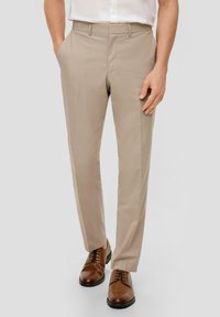 Pantalones de vestir color beige con una textura suave, corte ajustado y bolsillos laterales, combinados con zapatos de cordones marrones, exhibidos sobre un fondo neutro.