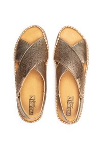 Sandales en cuir marron avec un design à brides croisées, des détails en relief et une semelle intérieure rembourrée. Présente des bords tressés et une forme de toe arrondie.