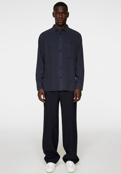 Navy button-up shirt in lightweight fabric with a chest pocket, paired with loose-fitting navy pants and white sneakers.