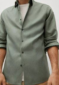Lichtgroene blouse met lange mouwen, gemaakt van een gladde stof, voorzien van een klassieke kraag, zwarte knopen en opgerolde mouwen.