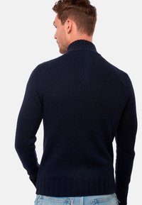 Pull en maille bleu marine avec un col côtelé haut, une coupe ajustée et des manches longues ; présente un ourlet côtelé en bas.