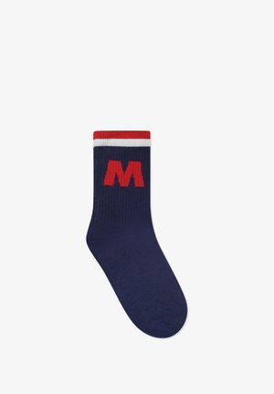 Calzino blu navy con strisce rosse e bianche nella parte superiore, dotato di un grande logo rosso a forma di "M" sul lato. Tessuto lavorato a maglia con texture a costine.
