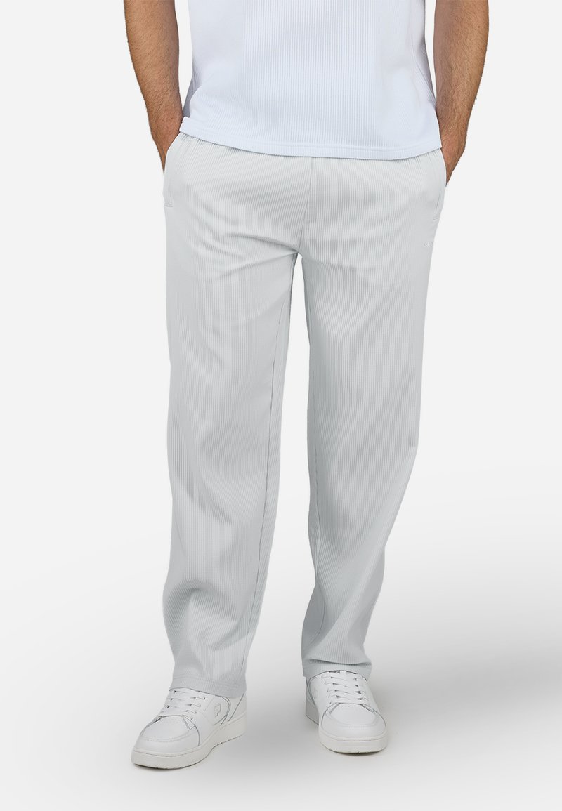 Pantaloni a coste grigi chiari con gamba dritta, dotati di tasche laterali, abbinati a sneaker bianche per un look casual.