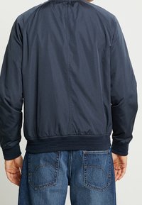 Marine Bomberjacke aus glattem, leichtem Stoff; verfügt über gerippte Bündchen und Saum, hat eine lockere Passform und ein minimalistisches Design.