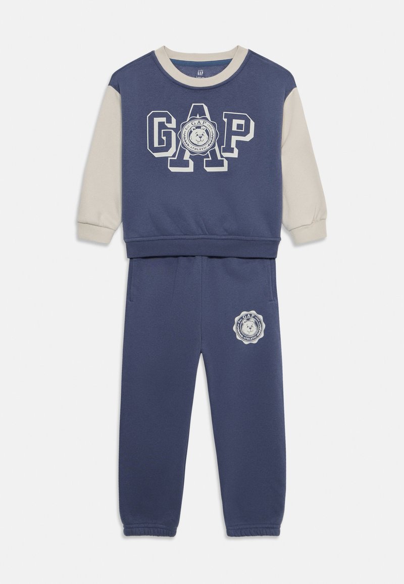 Set trenirke in hlače v mornarsko modri in kremni barvi. Zgornji del ima v beli barvi logo "GAP". Hlače imajo logotip leva na nogi. Mehka tkanina.