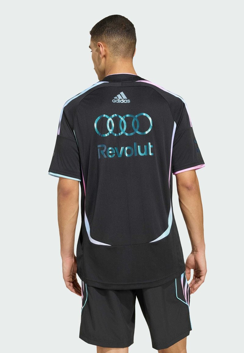 Uomo che indossa una maglia sportiva e pantaloncini neri Adidas con i loghi Audi rings e Revolut sulla schiena, in piedi con la schiena rivolta alla telecamera.