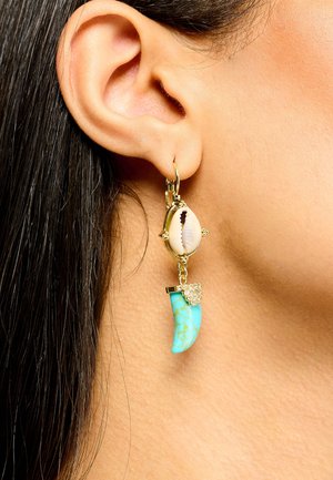 Boucle d'oreille créole en or avec un coquillage blanc et un pendentif en forme de corne turquoise orné de petits cristaux.