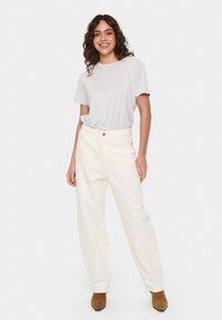 Tricou gri deschis combinat cu pantaloni albi cu talie înaltă și laturi largi. Botine maro cu toc completează ținuta. Emite un design minimalist.