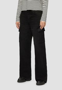 Pantalons cargo noirs à jambe large en denim, dotés de poches latérales et d'une finition texturée, associés à un haut à rayures à manches longues.