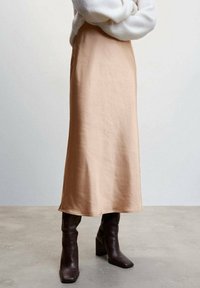 Satin midi skirt in soft peach, featuring a smooth texture and an A-line design. Paired with dark brown heeled boots.