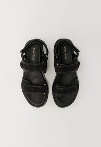 Sorte sandaler med to teksturerte stropper, justerbare spenner og en glatt såle. Har detaljer i gullfarge og en polstret fotseng.