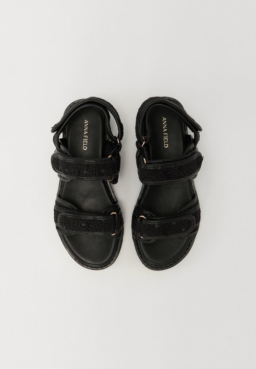 Mustad mustad kahe tekstuuriga rihmaga, reguleeritavate pannaldega ja siledal tallal. Omab kullatooni detailide ja pehmendatud sisetallaga.