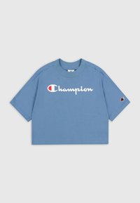 Camiseta corta azul de algodón, con un logo blanco de "Champion" y un pequeño emblema rojo y blanco en la manga. Mangas cortas.