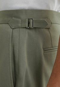 Pantalones de talle alto color verde oliva con cinturón de tela y hebilla plateada, combinados con una camiseta blanca de canalé.