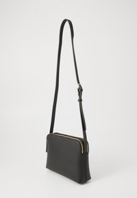 Sac à bandoulière en cuir noir avec une surface texturée, de forme rectangulaire et des accents de fermeture éclair dorés. Sangle fine ajustable en longueur.