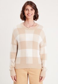 Beiger und weiß kariertes Sweatshirt aus weichem Strickmaterial mit gerippten Bündchen und Halskragen. Kombiniert mit hellen Cordhosen.