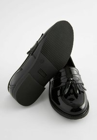 Mocasines de charol negro con suela de goma plana, que presentan un acento de flecos y detalles de costura, diseñados para la comodidad y la durabilidad.