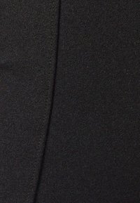 Tela negra con una textura suave que presenta un detalle de costura vertical, proporcionando una apariencia estructurada. Vista en primer plano de la superficie del material.