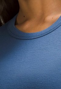 Top in maglia blu a coste con scollatura arrotondata e una texture morbida, caratterizzato da sottili variazioni di tono.