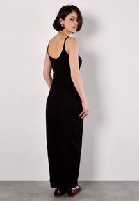 Abito maxi nero a coste con spalline sottili, design aderente e texture liscia, che arriva fino alle caviglie, abbinato a ballerine bordeaux.