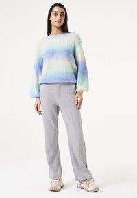 Pastellfarbener, sanft verlaufender Strickpullover mit lockerer Passform, rundem Ausschnitt und langen Ärmeln, kombiniert mit hellgrauen, elastischen Bundhosen und beigen Sneakers.
