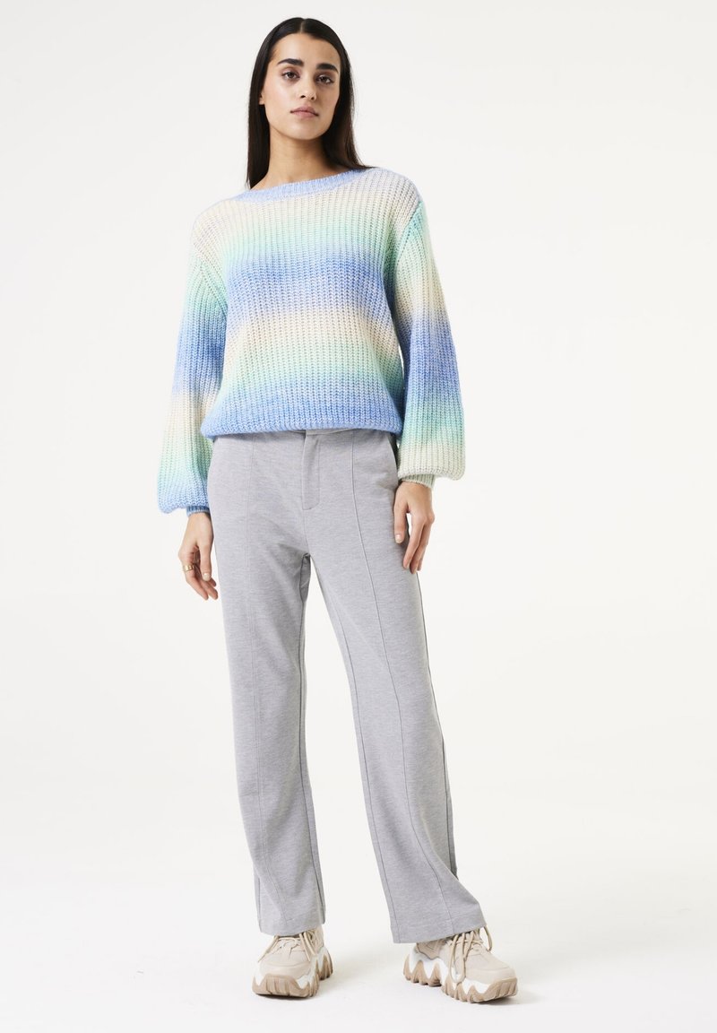 Pastellfarbener, sanft verlaufender Strickpullover mit lockerer Passform, rundem Ausschnitt und langen Ärmeln, kombiniert mit hellgrauen, elastischen Bundhosen und beigen Sneakers.