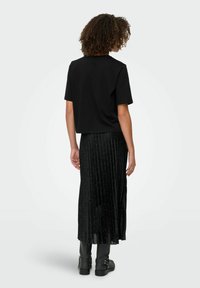 Sort cropped T-shirt med korte ærmer, parret med en sort plisseret nederdel med glitrende detaljer. Båret med sorte ankelstøvler.