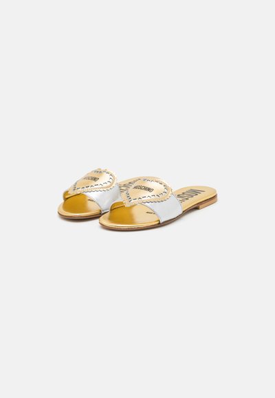 Metalliska silver- och guldslide-sandaler har en vågig kant, dekorativ sömnad och en tryckt logotyp på fotbädden. Platt sula.