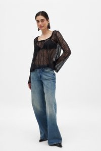 Zwarte kanten top met lange mouwen, voorzien van een ronde hals en een gestrikt detail aan de voorkant. Gemaakt in combinatie met hoog-waist, lichtblauwe spijkerbroeken.