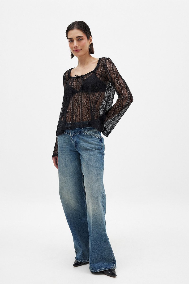 Zwarte kanten top met lange mouwen, voorzien van een ronde hals en een gestrikt detail aan de voorkant. Gemaakt in combinatie met hoog-waist, lichtblauwe spijkerbroeken.