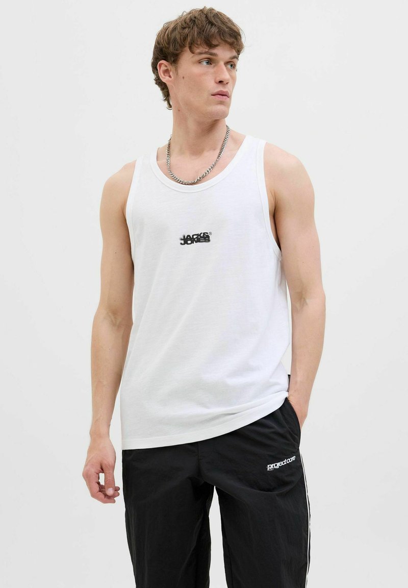 Witte katoenen tanktop met een ronde hals, voorzien van een klein zwart logo in het midden, gecombineerd met zwarte losse broek en een zilveren ketting.