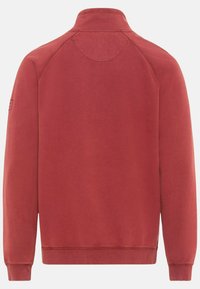 Sweat-shirt rouge avec un col montant, des manches longues et des poignets côtelés. Texture lisse, design minimaliste, et un petit logo accentué sur la manche gauche.