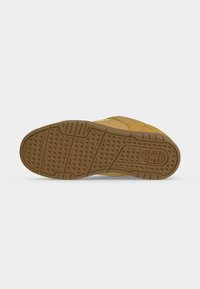 Semelle d'une basket couleur beige avec une bande de roulement en caoutchouc texturé et un petit logo géométrique près du talon.
