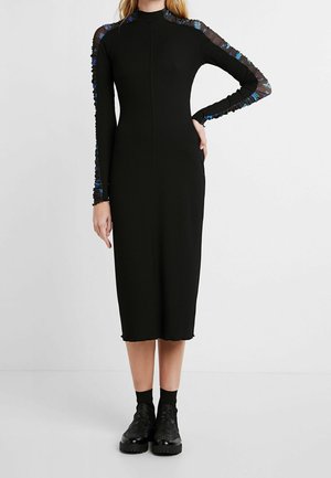 Robe midi noire côtelée à manches longues avec des accents floraux bleus transparents sur les épaules.Associée à des bottes noires épaisses.