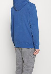 Sudadera azul con capucha, hecha de una tela suave y con puños acanalados. Combinada con pantalones cargo gris que cuentan con un detalle de bolsillo abotonado.