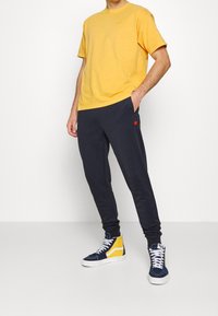 Žluté bavlněné tričko, tmavě modré tepláky s malým červeným a žlutým logem a modrožluté vysoké tenisky s bílými tkaničkami.