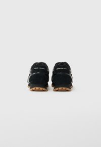 Baskets noires Armani Exchange avec semelles en gomme vues de l'arrière sur fond blanc uni.