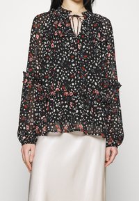 Černá šifonová blůza s vícebarevným květinovým potiskem, obsahující volány, výstřih ve tvaru klíče s tkaničkami a dlouhé rukávy se staženými manžetami.