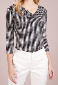 Zwart-wit geblokte lange mouwen top met een V-hals en geplooide details bij de hals, gecombineerd met witte broek.
