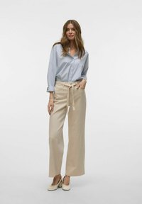 Ljusblå skjorta med knappar och uppvikta ärmar, matchad med beige vida byxor med dragsko i midjan och subtil textur.