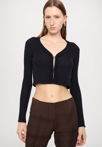Black ribbed cropped cardigan with long sleeves and a deep V-neck, featuring a front zipper closure. Soft, textured fabric.