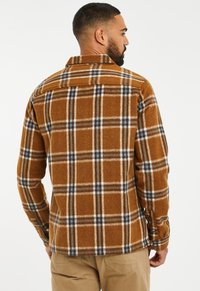 Brown plaid flannel shirt with blue and white accents. Button-down collar, long sleeves, and a slightly fitted design. Soft texture.