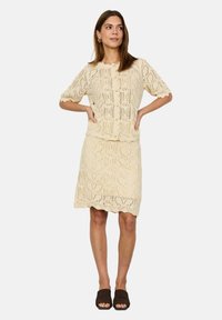 Gehaakte romige tweedelige outfit bestaande uit een top met korte mouwen en een kniebrede rok, die complexe kantpatronen met golfranden toont.