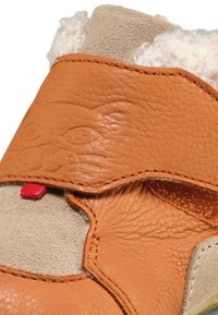 Zapato de cuero marrón con un acabado texturizado, con un diseño de cara de gato, lengüeta en rojo y un forro suave en beige.